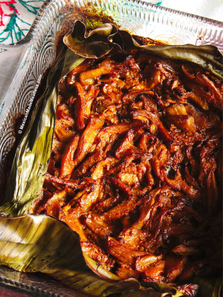 Close up view of roasted mushrooms cooked in banana leaf and cochinita pibil sauce.