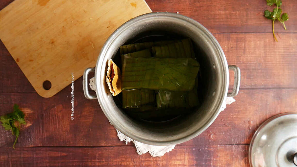 A small tamalera or tamale steaming pot filled with a stack of banana leaf tamales.