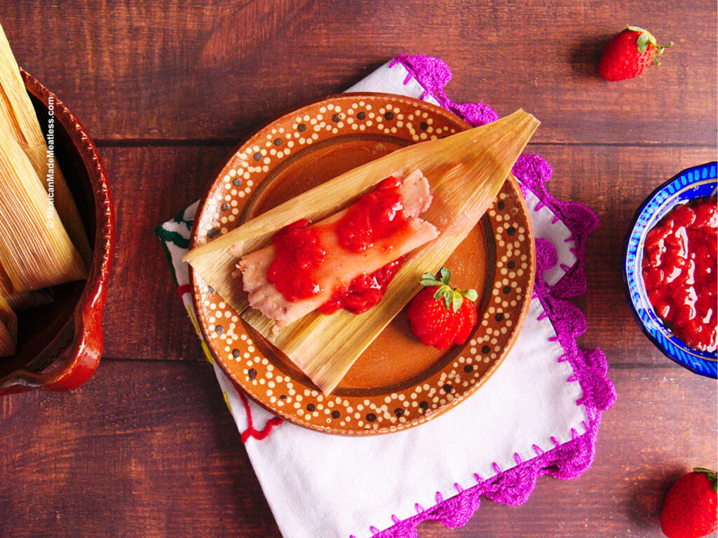 One cooked strawberry tamale laying on a corn husk and drizzled with homemade strawberry jam.