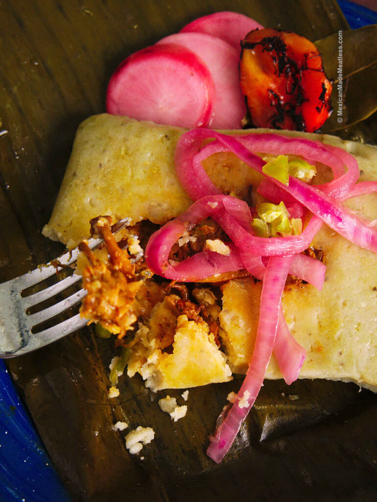 A plate lined with a banana leaf and one tamale on top of it filled with cochinita pibil. 