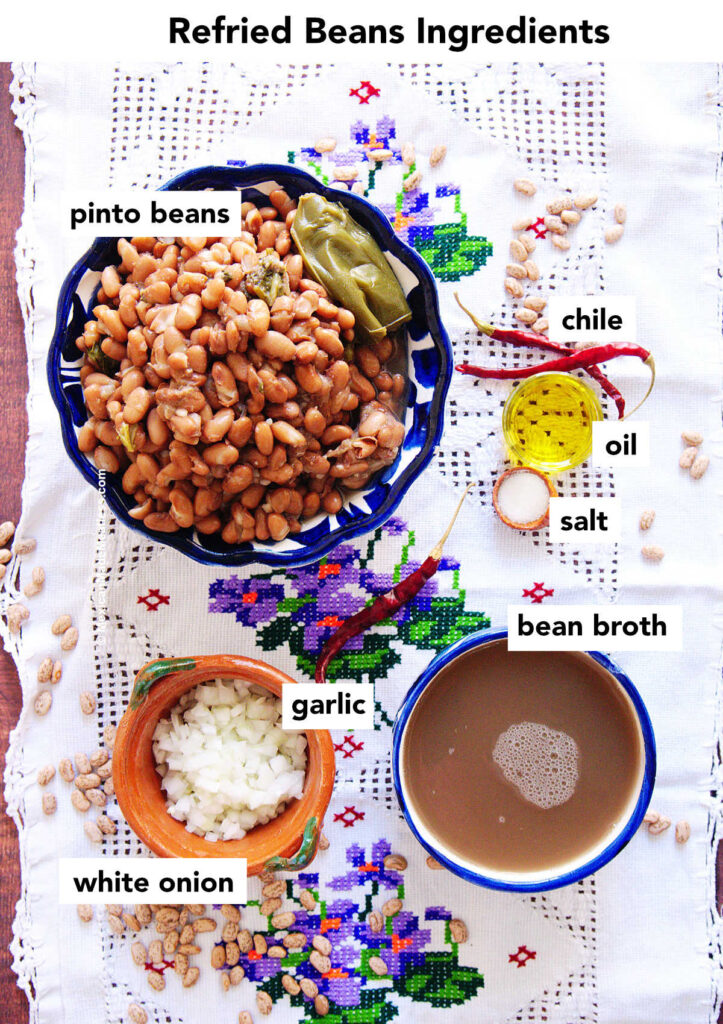 View from above of ingredients to make refried beans: pinto beans, onion, bean broth, oil, salt and red chilies.