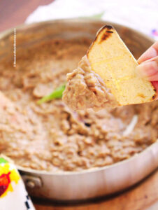 Close up view of a tortilla chip topped with creamy refried beans.