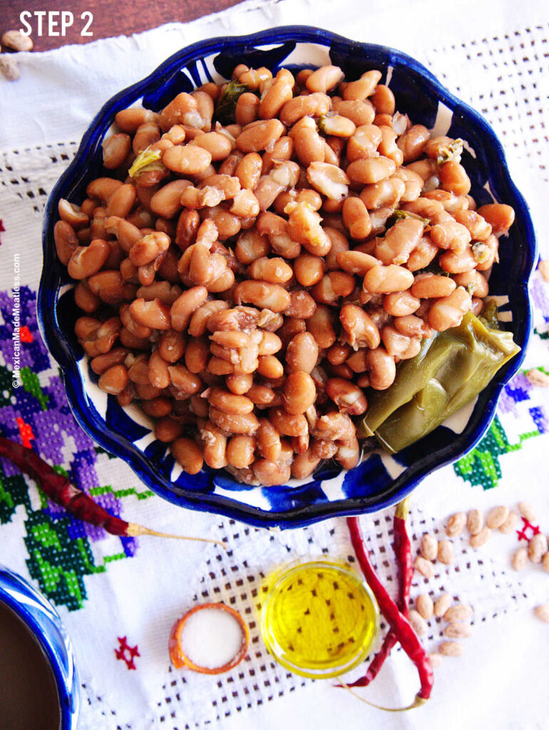 A blue and white bowl filled with cooked pinto beans sitting on a white linen. 