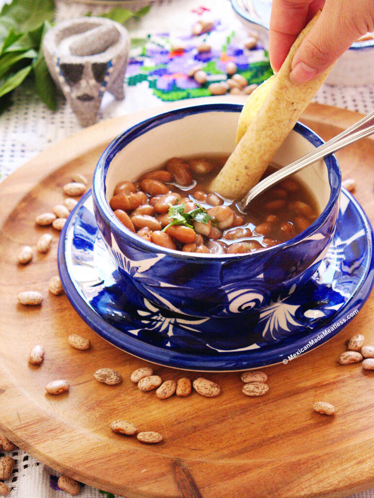 A small blue bowl filled with pinto beans and a rolled up corn tortilla being dipped into the bowl. 