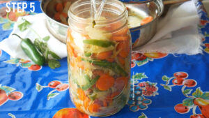 Filling a large mason jar with carrots, spices and pouring in pickling brine.