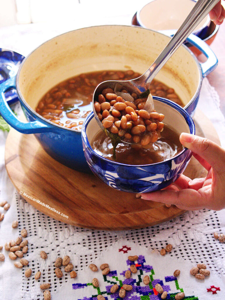 Using a ladle to pour cooked pinto beans into a small blue and white bowl. 