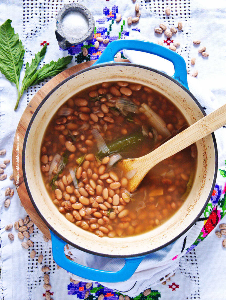 An enameled cast iron pot filled with cooked pinto bean sitting on top of a white table cloth.