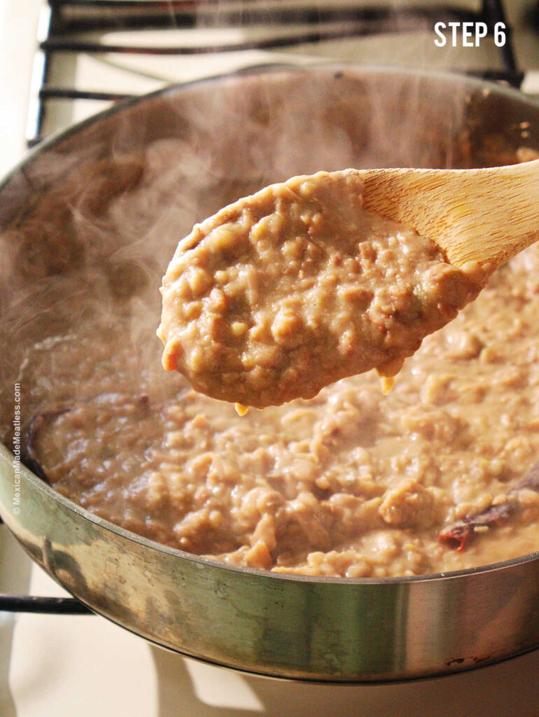 Closeup view of a wooden spoon filled with refried pinto beans.
