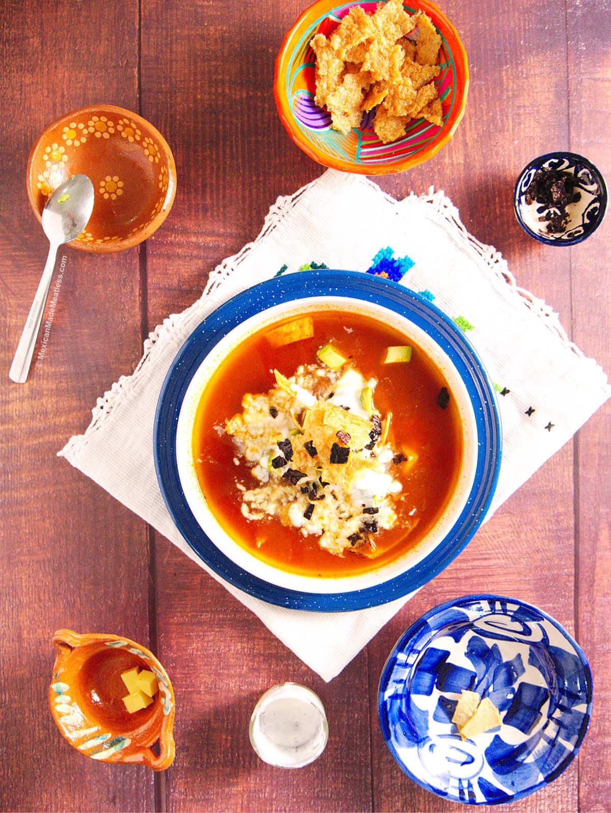 View from above of a white bowl filled with tortilla soup and small decorative bowls.