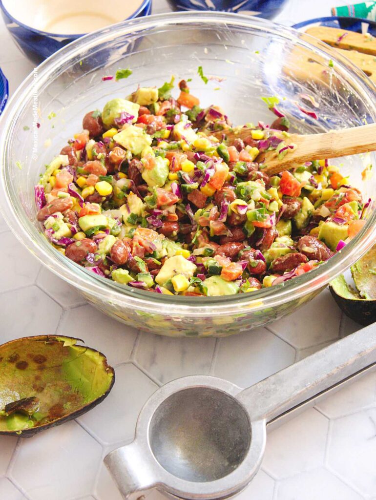 A large glass mixing bowl filled with bean salad with a creamy avocado dressing.