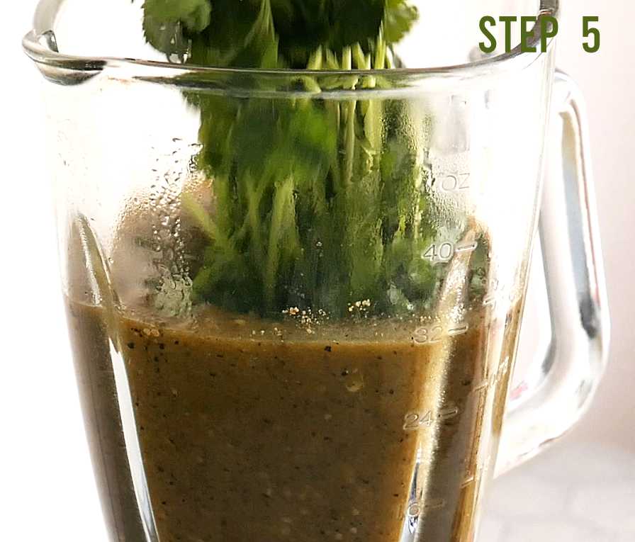 Adding fresh cilantro into a blender cup that's blending salsa verde.
