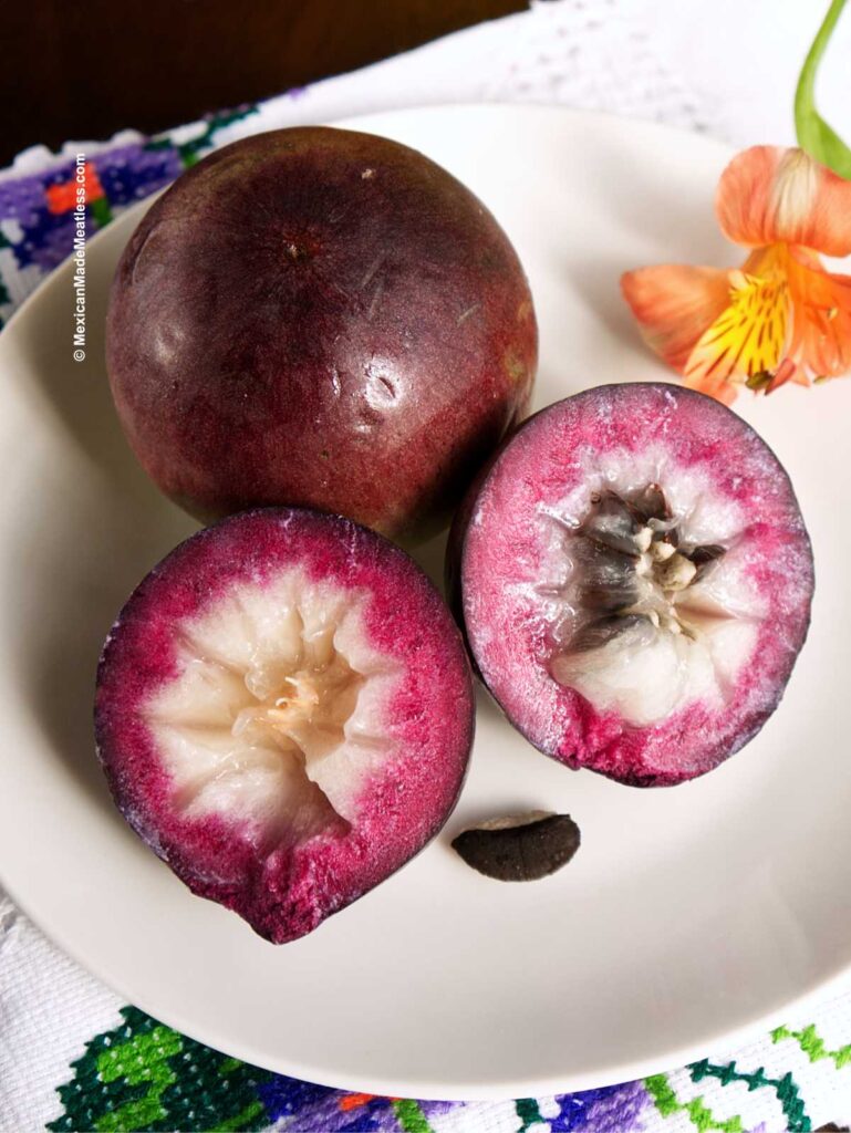 One whole and one sliced in half caimito fruit also known as star apple, on a white plate.