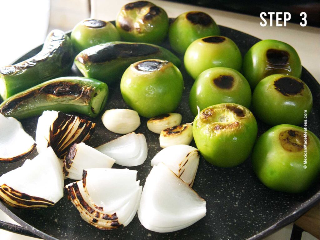 A hot griddle pan with charred tomatillos, jalapeno peppers, white onion and garlic.