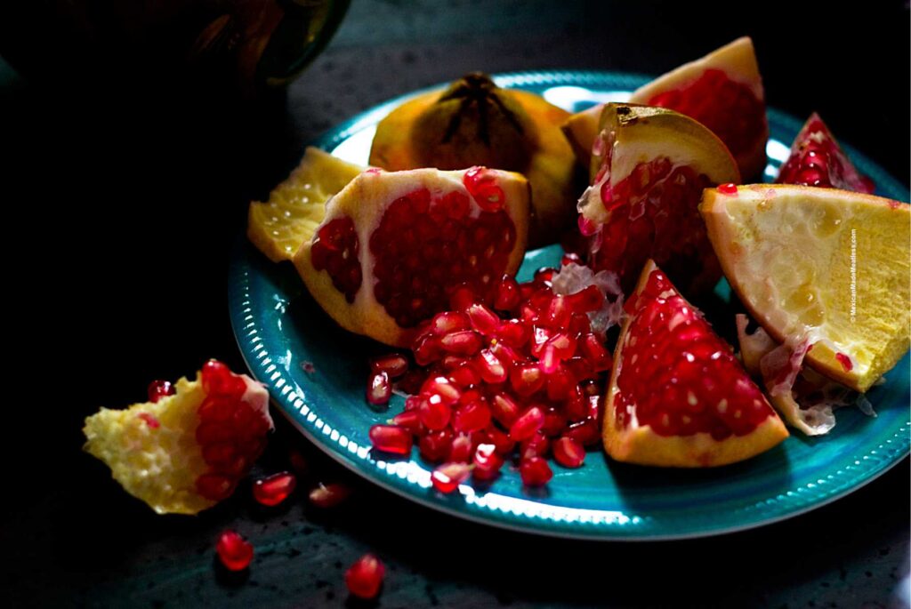 A pomegranate quartered and the seeds on a blue plate.