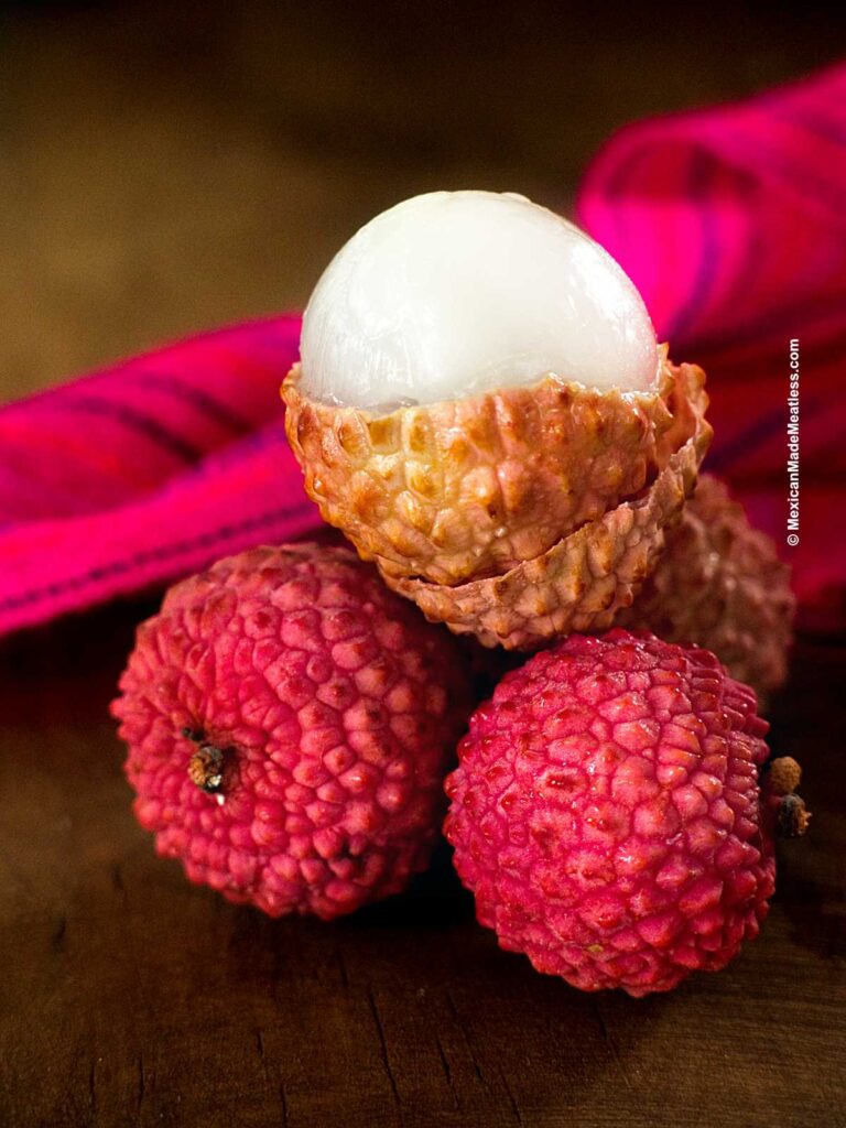 Three lychee stacked on top of each other. Two have their peel and one has been peeled to reveal the sweet juicy flesh.