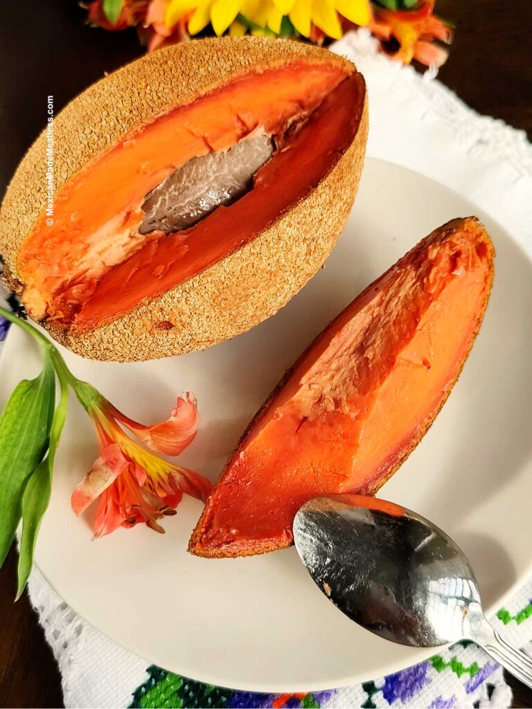 A mamey sapote on top of a white plate and with a wedge sliced off of it.