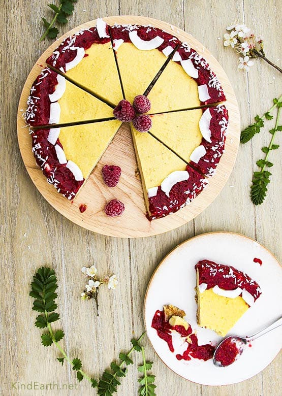 View of a whole vegan mango cheesecake with raspberry chia sauce on a wood platter.