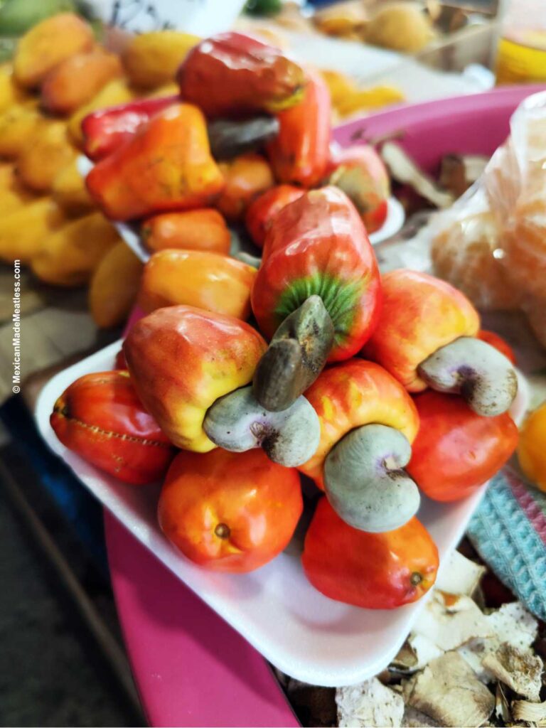 A pile of cashew fruit on a small white container in an open air Mexican market.