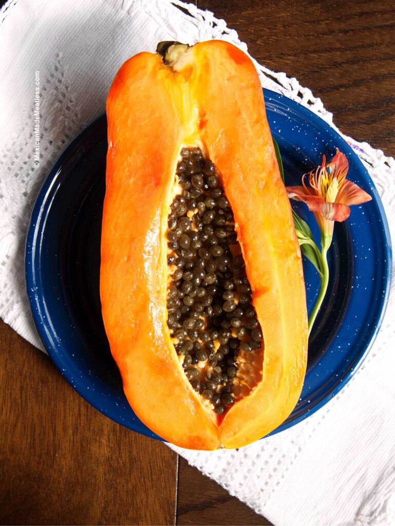 Half of a Maradol or Mexican papaya on a blue plate showing the small black seeds.
