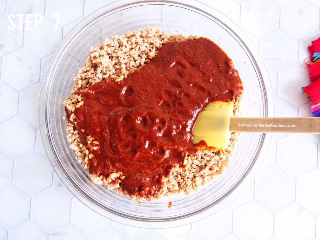 A glass bowl filled with hydrated soy crumbles and red chile sauce on top of it ready for mixing and making vegan soy chorizo.