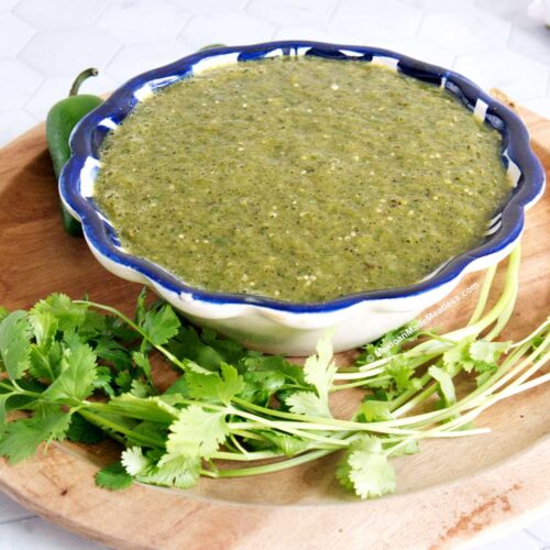 A blue and white bowl filled with roasted jalapeno salsa verde and there's fresh cilantro on the side.