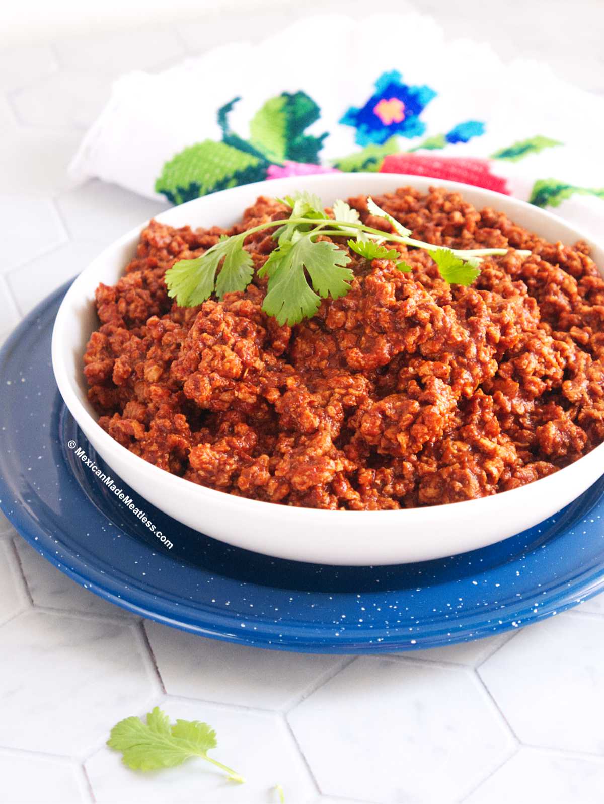 A white bowl placed on top of a blue plate and the bowl is filled with homemade Mexican vegan chorizo made from soy crumbles.