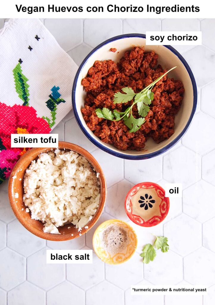 View from above of countertop with a bowl filled with vegan chorizo, another with crumbled silken tofu, a small one with oil and another with black salt.