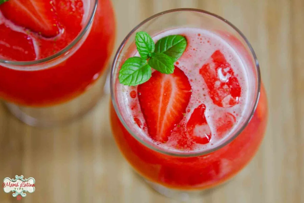View from above of a glass filled with strawberry agua fresca and inside are sliced strawberries and a sprig of mint.