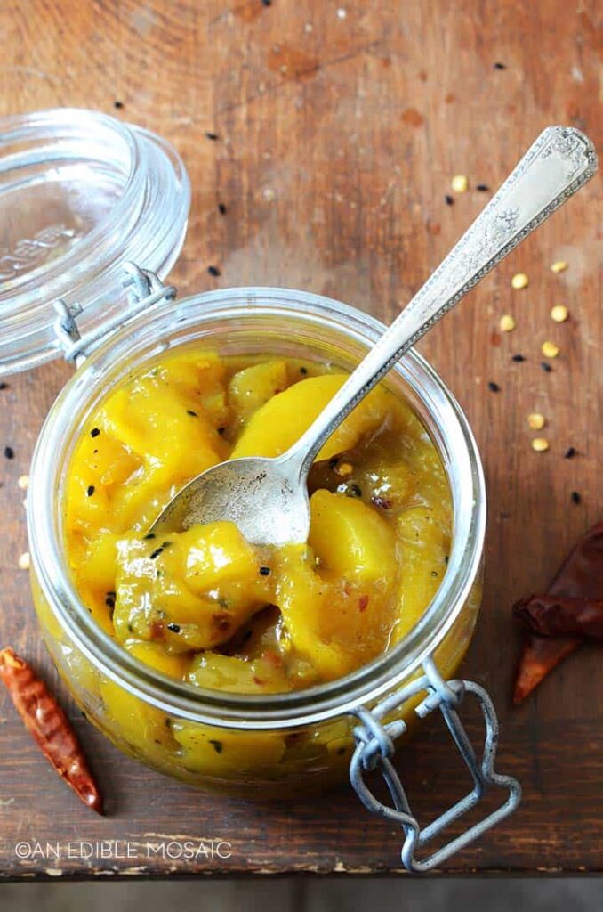 A small glass jar filled with Indian mango chutney and a spoon scooping some out.