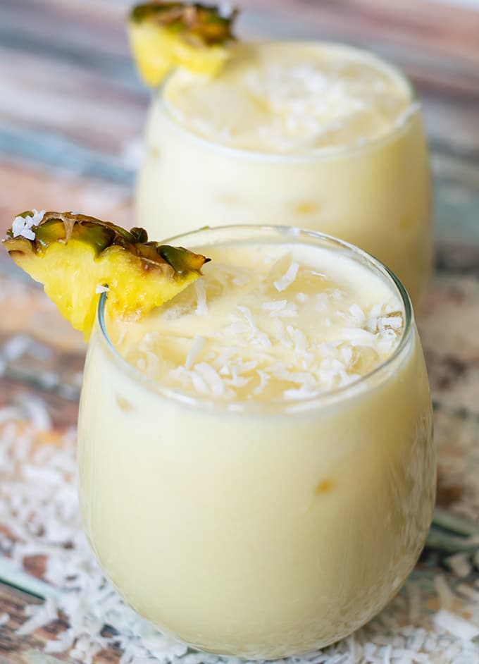 Two short glasses filled with pina colada agua fresca and topped with shaved coconut and a wedge of pineapple.