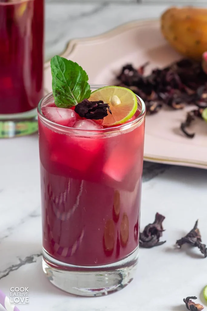 A glass filed with Prickly Pear Hibiscus Agua Fresca and topped with a mint leaf, hibiscus flower and a slice of lime.