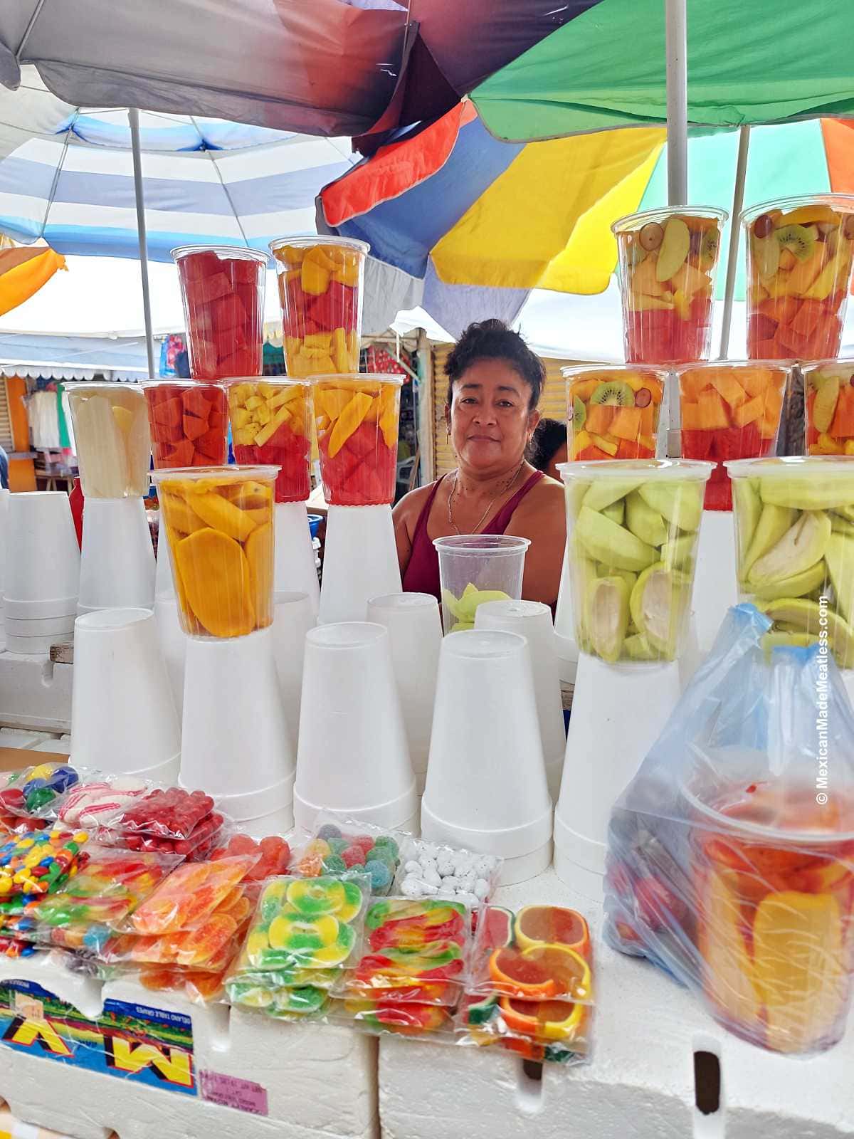 Photo of a woman vender in an open air market in Campeche Mexico selling cut up fruit.