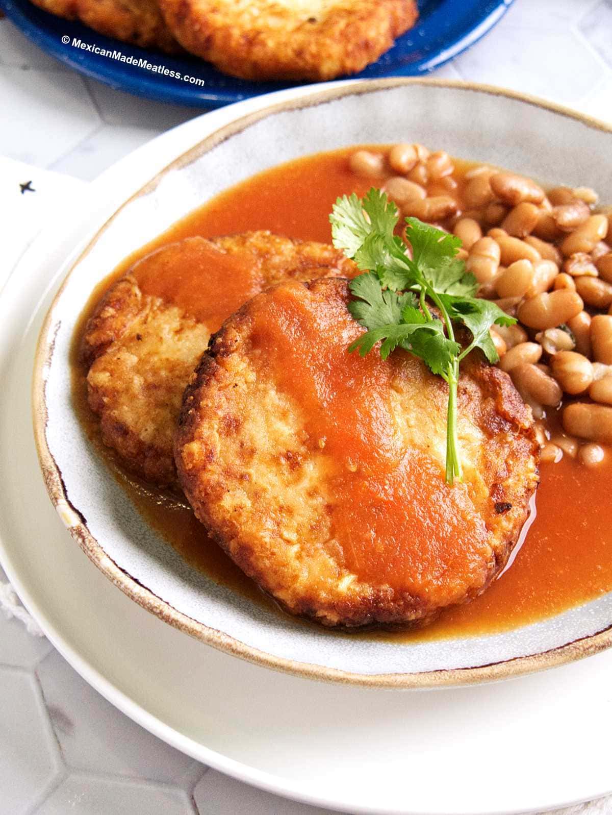 A white plate with tomato salsa and boiled pinto beans and two crispy Mexican potato cakes.