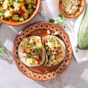 Two calabacita tacos with crumbled queso on a Mexican earthenware plate.