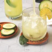 Pouring agua de pepino (cucumber agua fresca) into a small glass filled with ice cubes.
