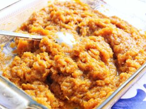 A close-up of a glass dish filled with thick homemade pumpkin puree for empanadas, with a spoon resting inside the mixture.