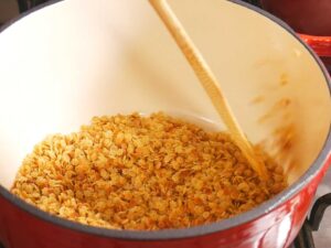 A large red pot filled star pasta being stirred with a wooden spoon, for sopa de estrellas.