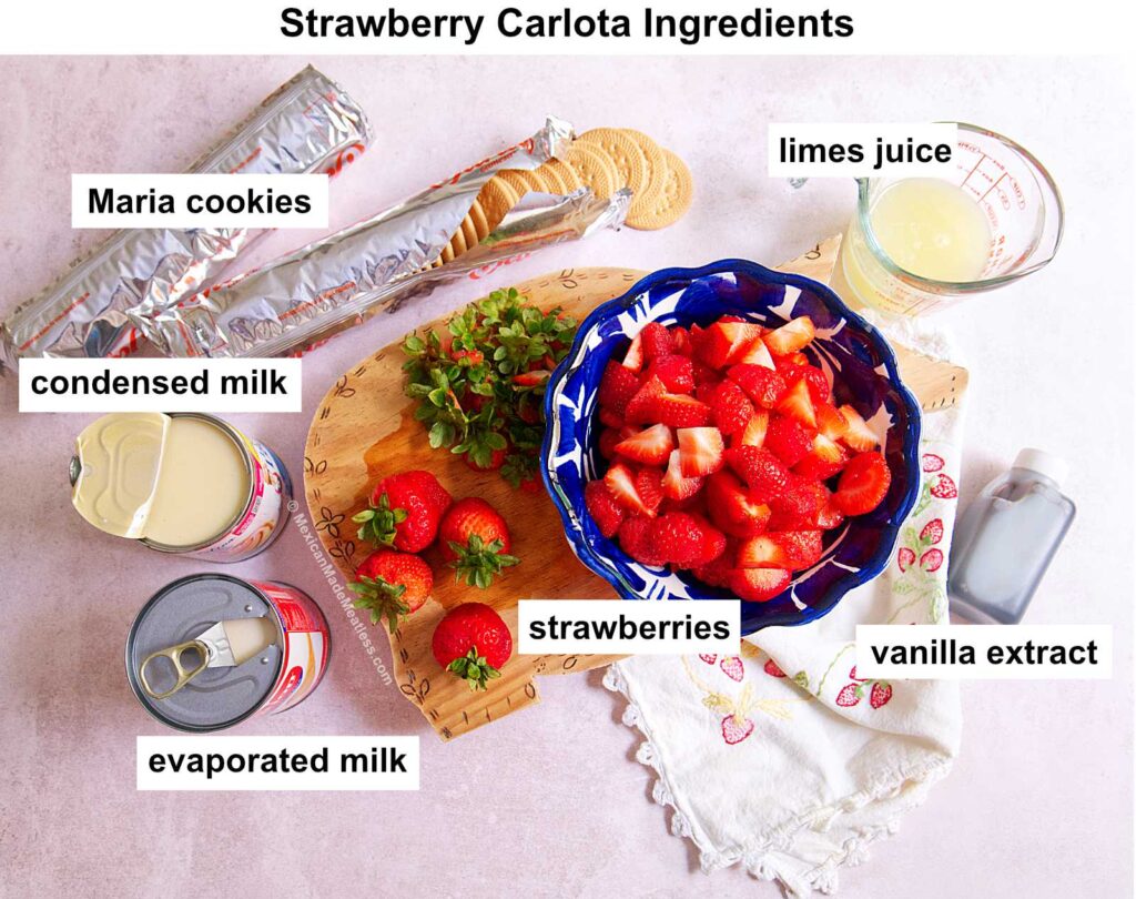 A top view of ingredients for Carlota de Fresa: Maria cookies, lime juice, condensed milk, evaporated milk, fresh strawberries, and vanilla extract, all arranged on a table with labels.