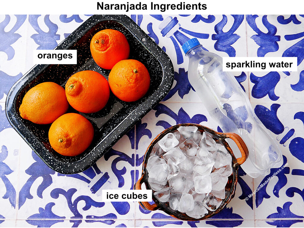 A tray of four oranges, a bottle of sparkling water, and a bowl filled with ice cubes are labeled as ingredients for naranjada, displayed on a blue and white patterned surface.